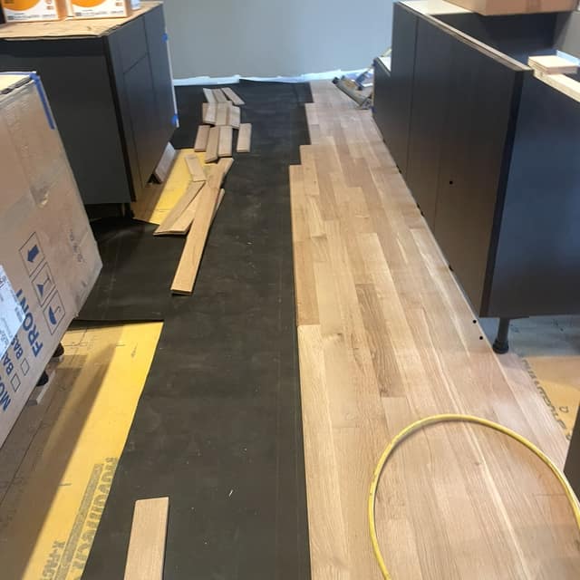 Hardwood planks being installed over underlayment in a kitchen