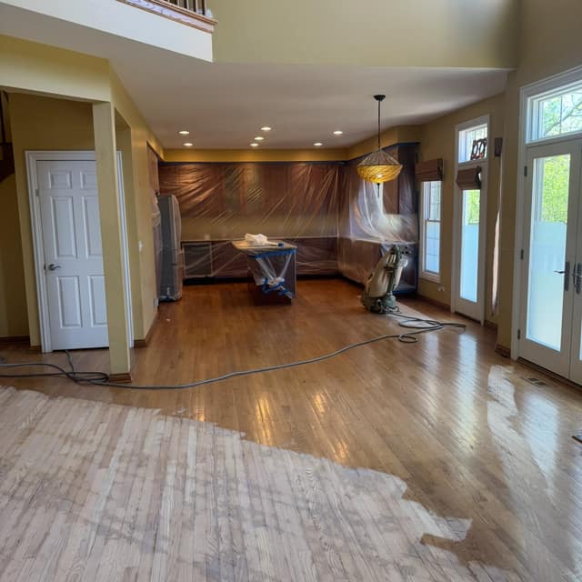 Floor mid-refinish — sanded bare wood in front, the old finish beyond, kitchen masked off for dust
