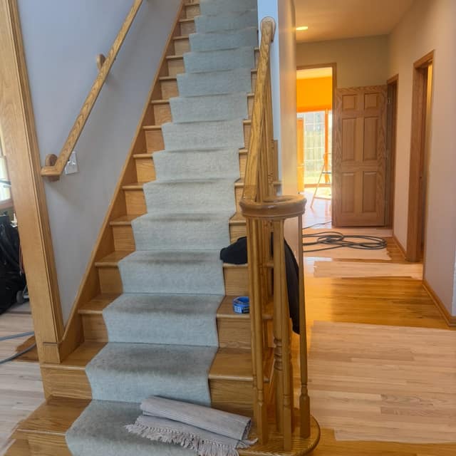 Wood staircase with a runner beside refinished pale wood floors
