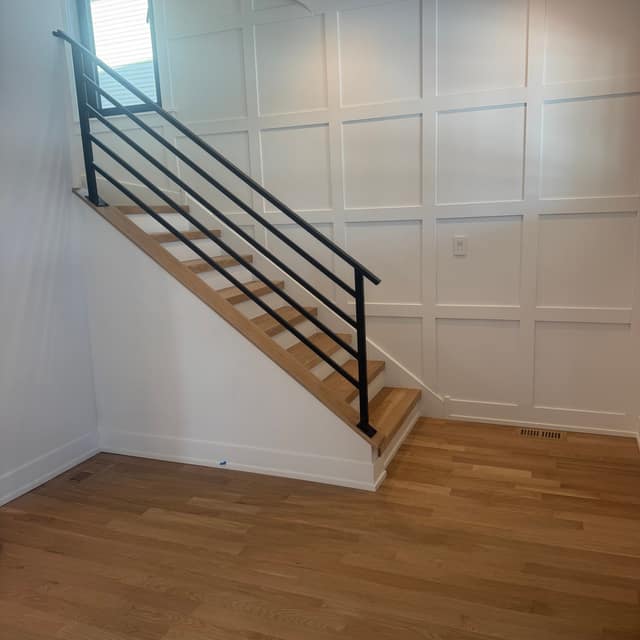 Modern staircase with a black metal railing over a light wood floor